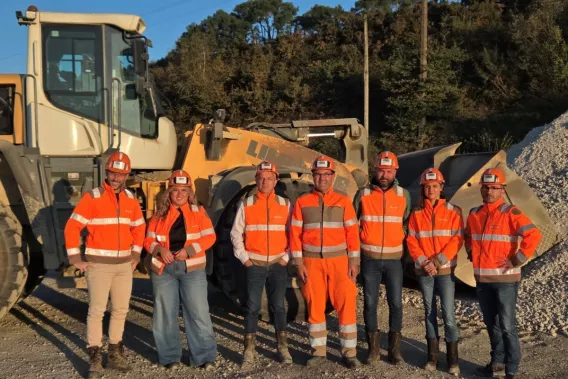 Équipe de collaborateurs Nexstone de la carrière de Plumelin portant des équipements de protection individuelle devant un chargeur sur pneus, sur le site d'exploitation.
