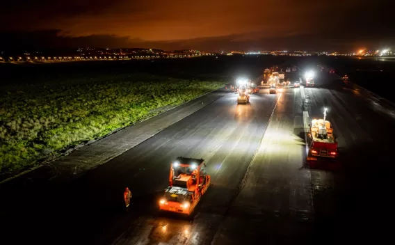 Travaux de voirie de nuit avec engins de chantier et mise en œuvre d’enrobé sur chaussée en infrastructure routière.
