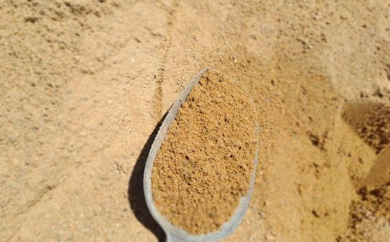 Sable granulaire utilisé en construction et aménagement, présenté à la pelle sur un stock de matériau minéral