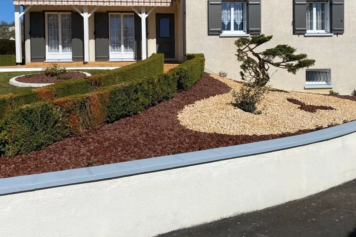Aménagement paysager avec pouzzolane en paillage minéral, utilisé pour structurer des massifs, limiter les mauvaises herbes et favoriser l’infiltration de l’eau autour d’une habitation.