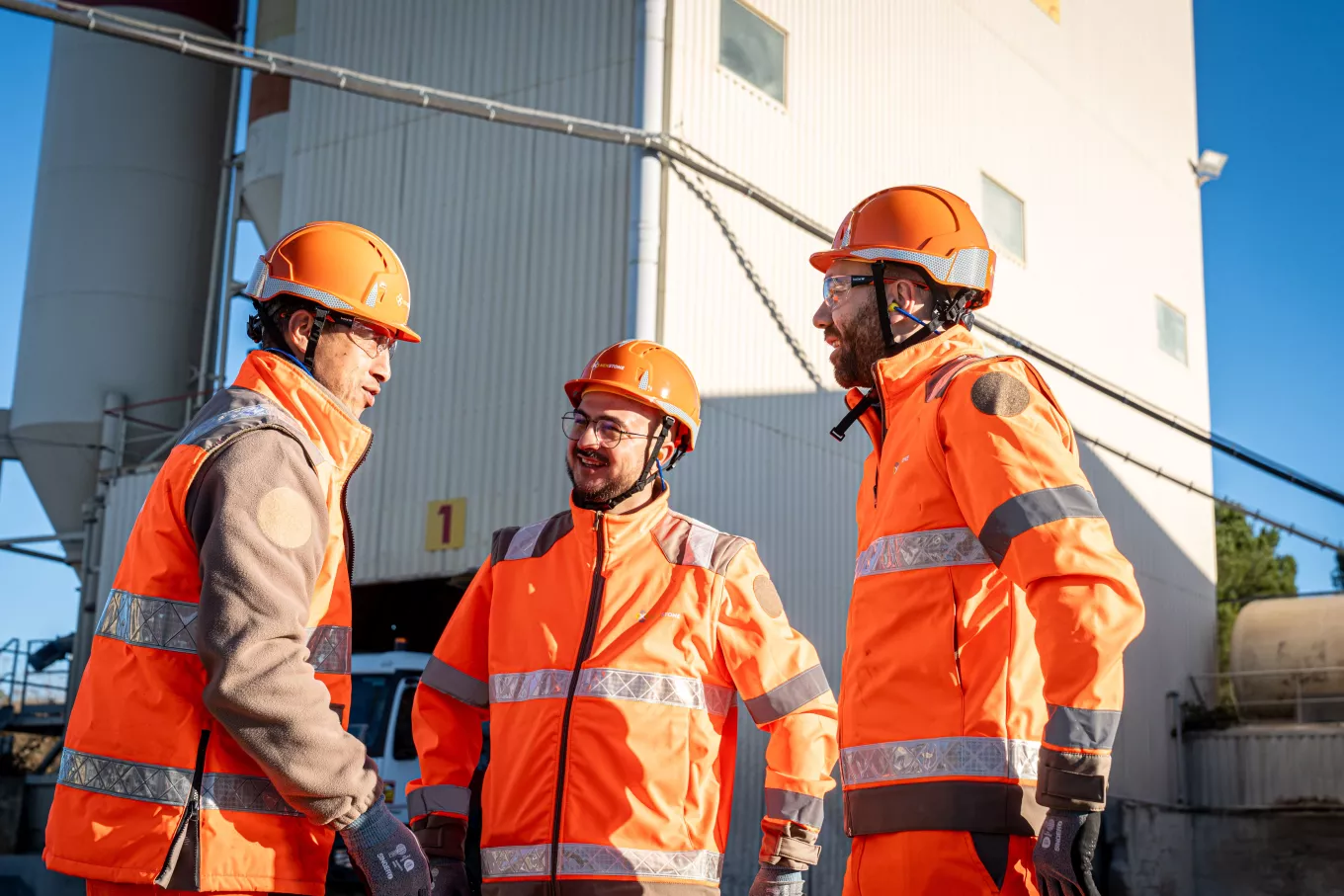 Collaborateurs sur la centrale à béton de Vendargues portant des équipements de protection (casques, tenues haute visibilité) en échange sur site de production, illustrant la coordination des opérations et des équipes.