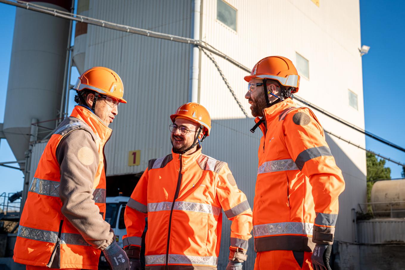 Collaborateurs sur la centrale à béton de Vendargues portant des équipements de protection (casques, tenues haute visibilité) en échange sur site de production, illustrant la coordination des opérations et des équipes.