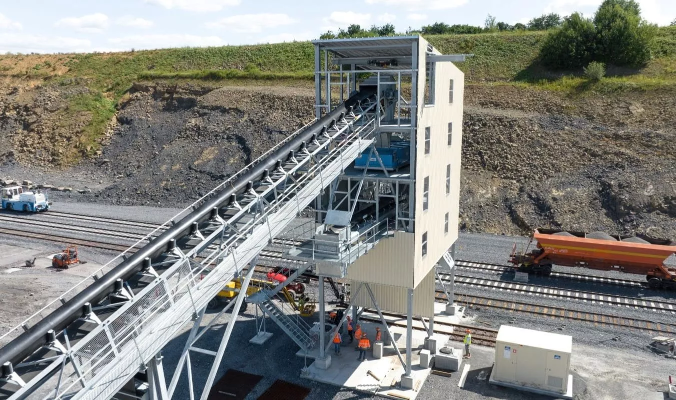 Installation industrielle de logistique rail avec convoyeur et chargement de matériaux sur wagons.