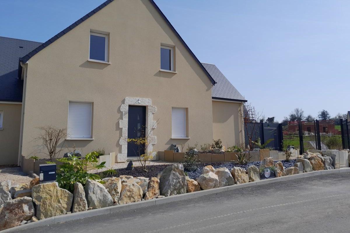 Blocs rocheux décoratifs en pierre naturelle aménagés devant une maison individuelle pour structurer les espaces extérieurs et stabiliser les abords de voirie.