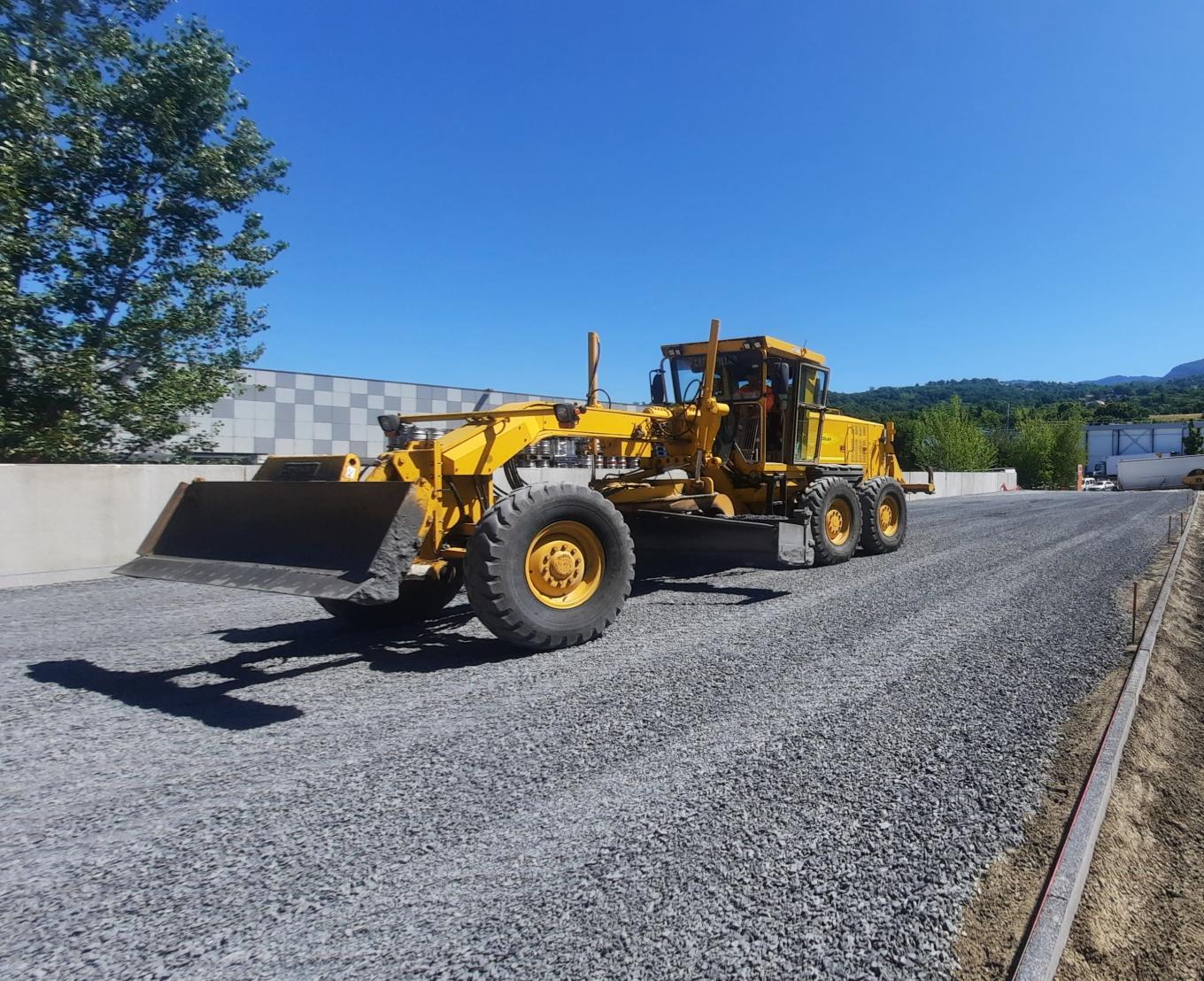 Niveleuse répartissant et nivelant une couche de graves sur une plateforme de chantier en préparation d’infrastructure.