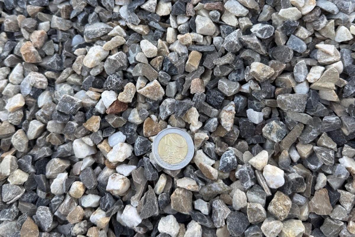 Granulat concassé de calibre intermédiaire, présenté avec une pièce de monnaie pour illustrer la granulométrie du matériau.