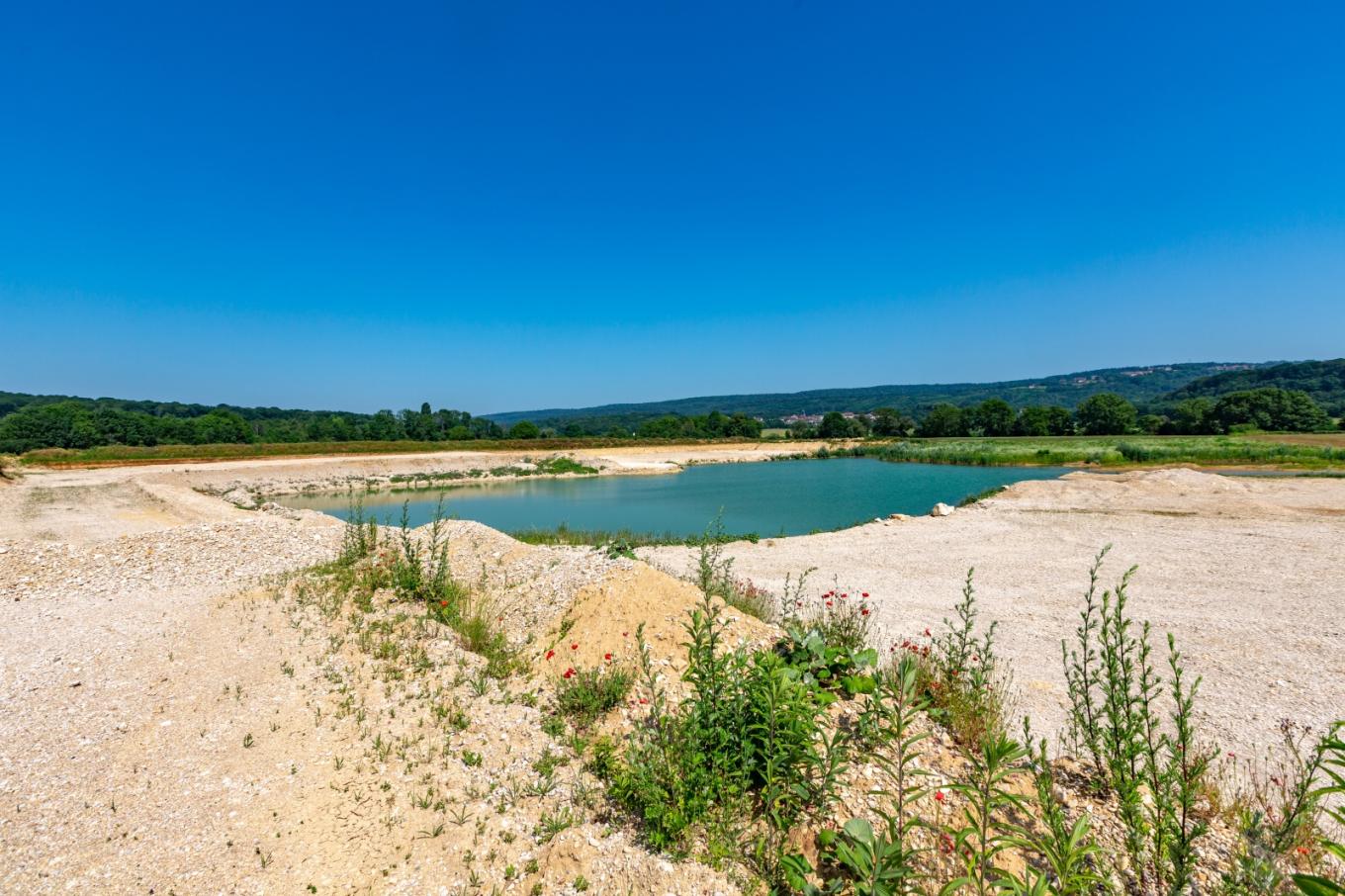 Vue de la gravière d'Osselle dans le Doubs, avec un plan d'eau entouré de bancs de sable, illustrant un site d'extraction de granulats favorable à la biodiversité