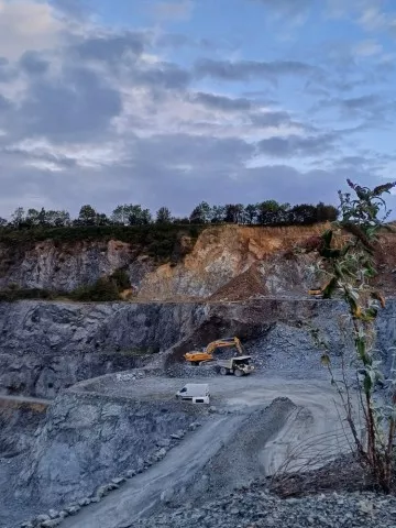  Fronts de taille en gradins à la carrière de Montsurvent, avec une pelle mécanique et un tombereau sur une plateforme d’extraction.