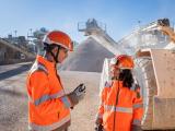 Deux collaborateurs Nexstone en tenue de sécurité haute visibilité échangeant sur un site de production de granulats, avec engins et stocks de matériaux en arrière-plan.