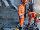 Deux collaborateurs Nexstone en tenue de sécurité haute visibilité réalisant des opérations de manutention et de contrôle au sol sur un site de production de béton.