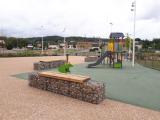 Aire de jeux aménagée avec bancs en gabions et revêtement minéral pour espace public.