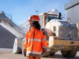Collaboratrice Nexstone en carrière avec équipements de protection, devant engin de manutention et stock de granulats.