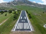 Vue aérienne de la piste rénovée de l’altiport Henri Giraud à l’Alpe d’Huez, entourée par le paysage montagneux.